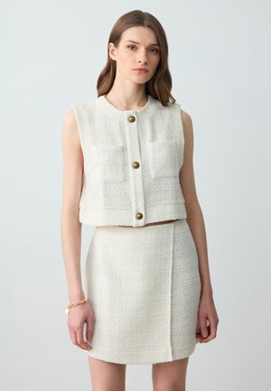 White tweed crop vest with four front pockets, gold button closures, paired with a matching mini skirt featuring a side seam detail.