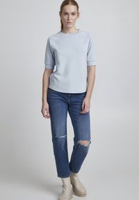 Top scurt de culoare albastră deschisă cu guler rotund, asortat cu blugi albaștri deteriorați și bocanci de gleznă crema. Material neted și croială lejeră.
