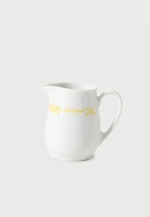 White ceramic milk jug with handle, spout, and yellow checkered pattern with café name on the side.