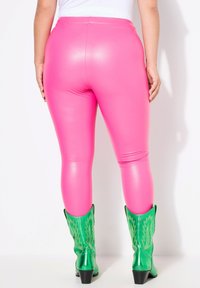 Leggings rosa aderenti realizzati in materiale lucido, abbinati a stivali da cowboy verde brillante con cuciture decorative e tacco a blocco.