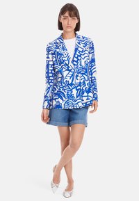 Blazer in Blau- und Weiß mit Muster und Reverskragen, kombiniert mit Denim-Shorts. Mit auffälligen abstrakten Designs und leichtem Stoff.