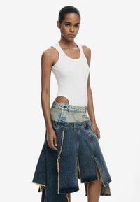 Top aderente bianco a righe con scollo rotondo abbinato a una gonna di jeans blu con orlo sfilacciato e design con tagli laterali.