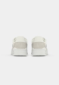 White sneakers with a suede grey back accent, rounded toe, textured upper, and rubber sole, featuring a minimalist design and no visible branding.