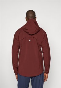 Burgunderrote wasserdichte Jacke mit Kapuze, die eine glatte Textur, subtile reflektierende Akzente und ein geschwungenes Saumdesign aufweist.