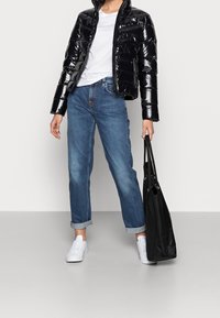 Czarna, błyszcząca kurtka puchowa, w zestawie z podwiniętymi niebieskimi dżinsami. Biała koszulka i białe trampki, trzymając czarną torbę na ramię.