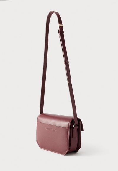 Ορθογώνια τσάντα ώμου από σκούρο βουργουνδί δέρμα με ρυθμιζόμενο λουράκι και κλείσιμο με καπάκι, μινιμαλιστικός σχεδιασμός, με ανάγλυφο το όνομα της μάρκας στο μπροστινό μέρος.
