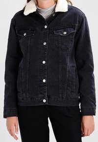 Svart denimjacka med fårskinnskrage, tryckknappar, två bröstfickor och en strukturerad passform; har en mjuk yta och en avslappnad design.