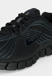 Μαύρο αθλητικό παπούτσι Nike με υφασμάτινη επάνω επιφάνεια, ευέλικτη τμηματική σόλα, μαύρα κορδόνια και ανακλαστική λωρίδα στη γλώσσα.