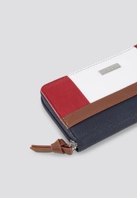 Portefeuille avec des sections en cuir rouge, blanc et bleu marine, accents marron, surface texturée, fermeture zippée et un petit détail de logo en métal.