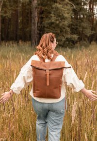 Šviesiai rudos odinės kuprinės dizainas su viršūnės suka ir reguliuojamomis petnešomis, užsegamas dirželiu. Dėvima su šviesiu bluzonu ir džinsais.