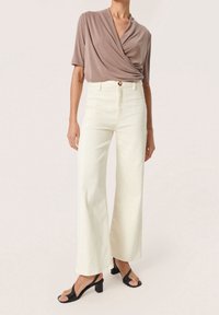 Ljust beige omlott-topp med korta ärmar, kombinerad med högmidjade, vida vita denimjeans och svarta klacksandaler.