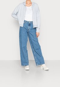 Sudadera azul clara con cremallera, camiseta blanca texturizada, jeans de mezclilla de tiro alto y de pierna ancha, y botas blancas hasta el tobillo. Atuendo simple y casual.