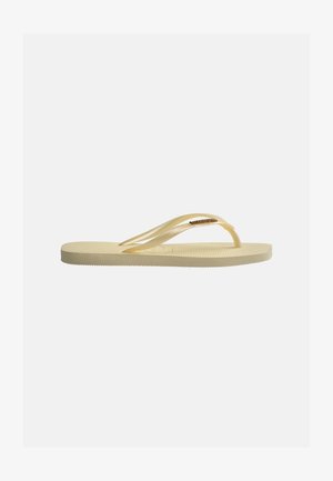 Enkelt beige flip-flop med mønstret sål og tynde stropper, med en lille guldfarvet mærkelogo på stroppen.