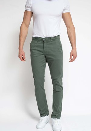 Pantalones chinos verdes de algodón con un corte ajustado, que cuentan con bolsillos frontales, cierre de botones y una textura suave. Combinados con zapatillas blancas.