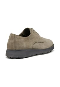 Zapatos de ante gris con cordones, punta redondeada y una suela de goma negra con un patrón de agarre texturizado, vistos desde el lado y la parte trasera.