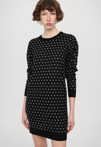 Abito nero in maglia con scollatura rotonda e maniche lunghe, caratterizzato da motivi circolari in pizzo bianco su tutta la superficie. Tessuto morbido, forma leggermente aderente.