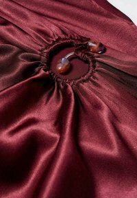 Tissu satin bordeaux profond rassemblé autour d'un fermoir métallique rond avec deux embouts marbrés marron et violet.