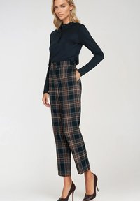 Granatowa koszula z długim rękawem w połączeniu z wysokim stanem spodni w kratę w kolorach zielonym, brązowym i kremowym, z bocznymi kieszeniami. Brązowe szpilki.