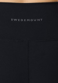 Black leggings with a smooth texture, featuring a wide waistband. "SWEDEMOUNT" logo in grey on the waistband. Flat seams visible.