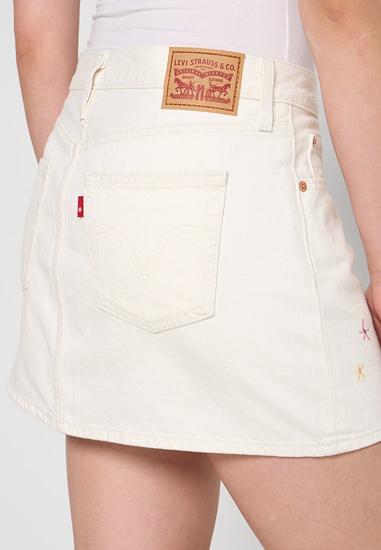 Mini-jupe en denim blanc à taille haute, dotée d'un patch en cuir de marque, de poches arrière et d'accents brodés multicolores.