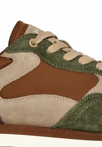 Gros plan sur une sneaker marron, beige et verte avec des panneaux en suède et en tissu, des lacets beiges et des coutures détaillées.