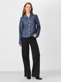 Blue lace-embroidered jacket with a rounded collar and button closure, paired with high-waisted black wide-leg jeans and black heels.