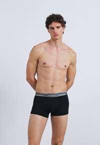 Fekete boxeralsó kontrasztos szürke derékpánttal. A szövet sima hatású, testhez álló kialakítású, amely kényelmet és tartást biztosít.