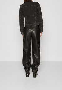 Svart denimjacka med synliga sömnadsdetaljer, ihop med högmidjade svarta läderbyxor. Båda har en avslappnad passform och slät textur.