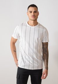 Camiseta blanca de manga corta con rayas verticales negras, escote redondo y textura suave. Combinada con pantalones cargo negros.