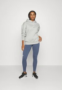 Sweat à capuche gris à coupe décontractée, associé à un legging bleu. Des chaussures de sport noires complètent la tenue.