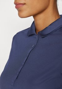 Polo shirt blu navy con colletto a camicia, caratterizzato da una texture liscia e sei bottoni lungo la patta, che mette in risalto una silhouette aderente.
