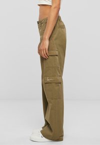 Cargo bukser i khaki bomuld med en løs pasform, der har flere sidelommer og et lille hvidt logo. Designet fremhæver funktionalitet og komfort.