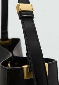 Zwarte leren tasriem met een gouden rechthoekige gesp, bevestigd aan een bijpassende zwarte leren tas tegen een effen achtergrond.