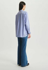 Chemise bleu clair à boutons, avec un pli au dos, des manches longues et une coupe décontractée, associée à un jean en denim foncé évasé.