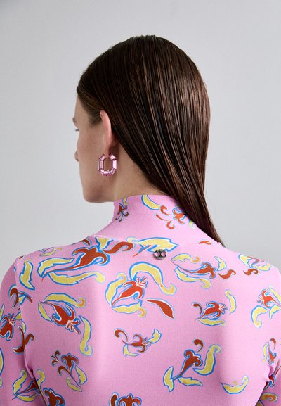 Roze bloemenpatroon top met een hoge hals, versierd met rode en blauwe ontwerpen, gecombineerd met geometrische roze oorbellen en een metallic accent aan de achterkant.