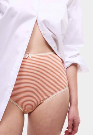 Gestreepte hooggeknipte onderbroek in oranje en roomkleur, met een delicate kantafwerking en een klein strikje in de taille. Model draagt een wit shirt.