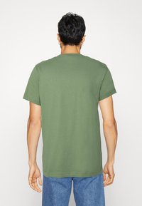 Camiseta verde de manga corta hecha de tela suave, con cuello redondo clásico y un corte relajado, que presenta una textura lisa y un diseño minimalista.