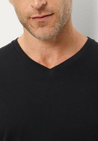 T-shirt nera in cotone a V con una texture liscia, una vestibilità aderente e senza motivi o accenti visibili, che mette in risalto un design semplice e minimalista.