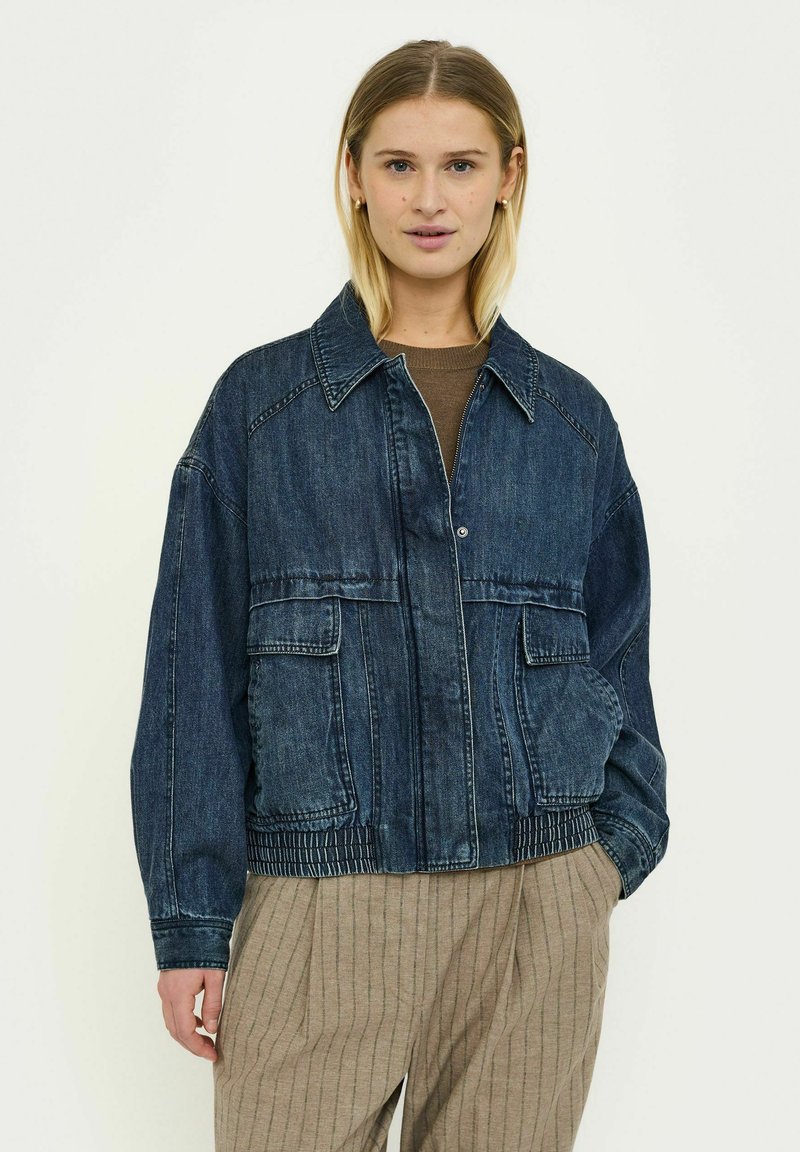 Jachetă din denim de culoare albastru închis, cu buzunare mari frontale, guler cu rever, tiv elastic și croială lejeră cu umeri lăsați.