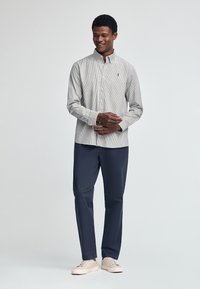 Skjorta med knappar, i tunna blå och vita ränder, lång ärm, krage. Matchas med marinblå byxor och ljusa sneakers.