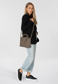 Borsa a tracolla in pelle color tan con manici superiori doppi e tracolla staccabile. Abbinata a un blazer nero, jeans azzurri chiari e sneakers nere.