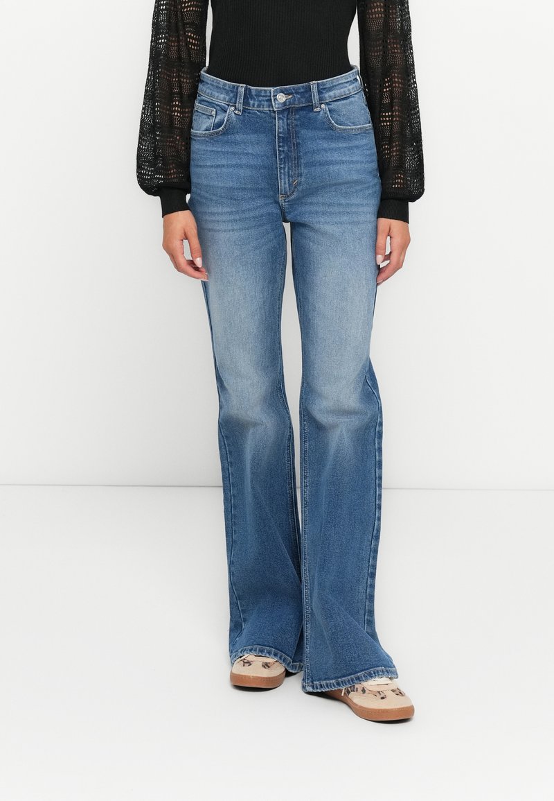 Uppvikta blå jeans i medelblå tvätt som har fem fickor, en knapp- och dragkedjestängning, samt diskret blekning vid låren.