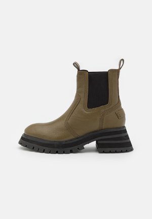 Bota corta de cuero verde oliva con paneles laterales elásticos, tacón elevado con franjas negras y grises, parte superior texturizada y lengüeta para tirar.
