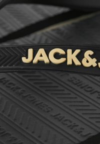 Μαύρη σόλα παπουτσιού με κίτρινο λογότυπο "JACK&" στο λουρί και υφασμάτινο μοτίβο με ανάγλυφες λεπτομέρειες του ονόματος της μάρκας.