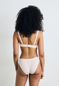 Vaaleanpunainen alusvaatesetti, joka sisältää säädettävillä olkaimilla varustetun bralette-topin, joissa on hakaskiinnitys, sekä yhteensopivat korkeavyötäröiset alushousut, joissa on sileä pinta.
