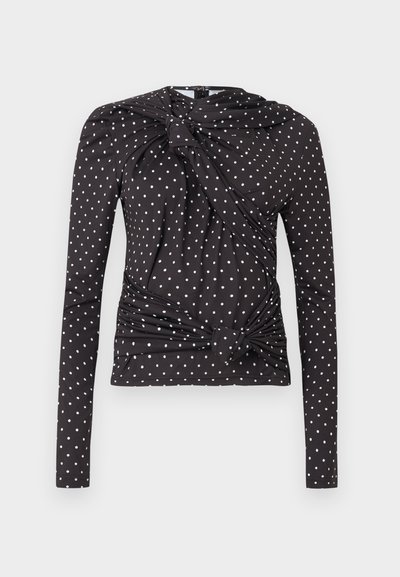 Μαύρο τοπ με μακριά μανίκια που διαθέτει λευκά πουά, σχεδιασμό με στρίψιμο μπροστά και κόμπο, και απαλό, ελαστικό ύφασμα για άνεση.