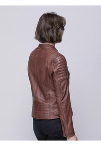 Brown leather jacket featuring a fitted design with ribbed accents on shoulders and quilted detailing at the waist, zippered cuffs.