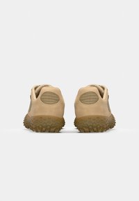 Beige athletic shoes with a textured suede finish, designed with a rubber outsole featuring prominent tread patterns and mesh accents.