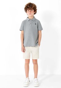 Polo gris à manches courtes et col, avec un petit logo marine, associé à un short beige clair et des baskets blanches.