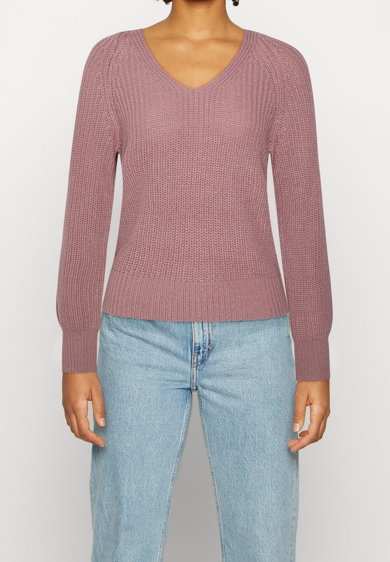 Maglione rosa lavorato a maglia con scollatura a V, texture a costine e maniche lunghe. Abbinato a jeans a vita alta di colore blu chiaro.